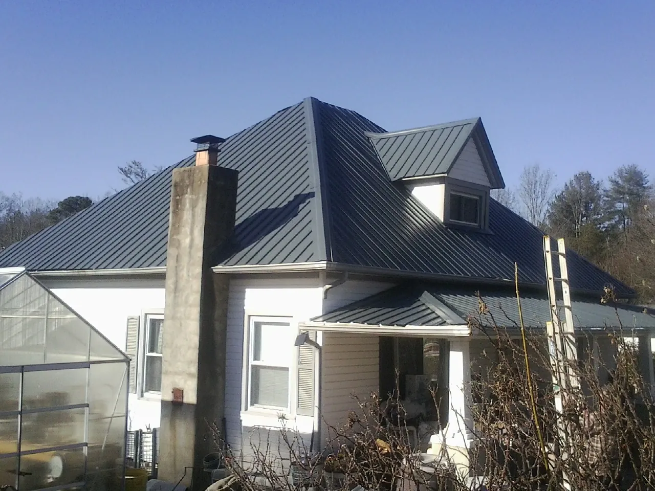 Dark blue standing seam metal roof on a white farmhouse with dormer — Slate & Tile Roof Repair by Roofing Brothers in Cripple Creek