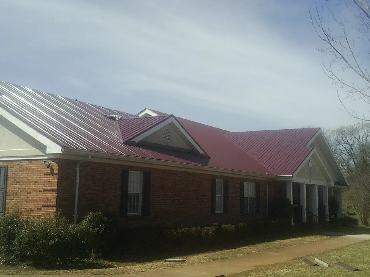 Red metal roof with gabled entries on a long brick building, from a Hail Damage Roof Repair job in Cripple Creek