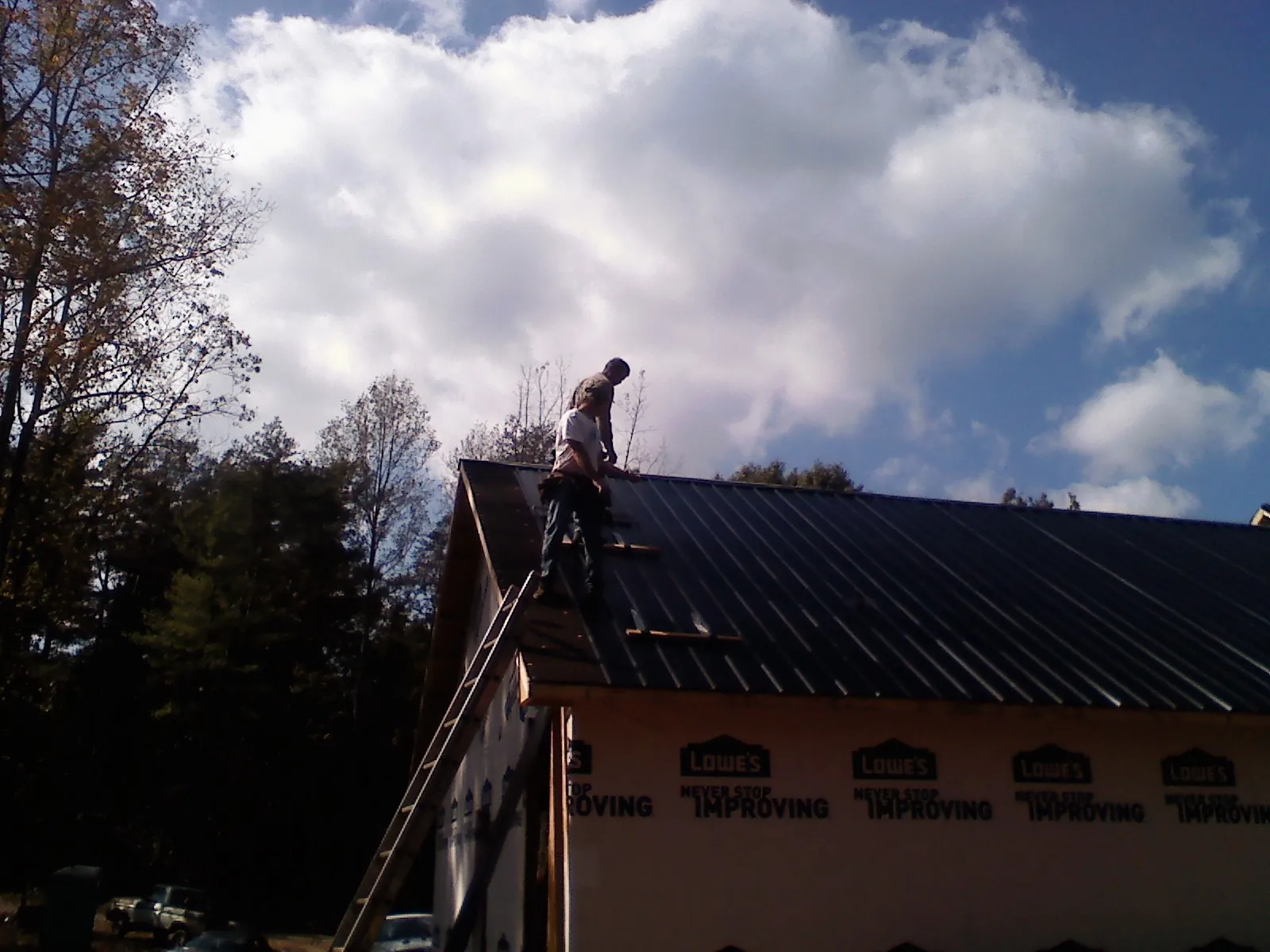 Roofer fastening dark metal panels high against a cloudy sky, from a Roof Inspection job in Cripple Creek