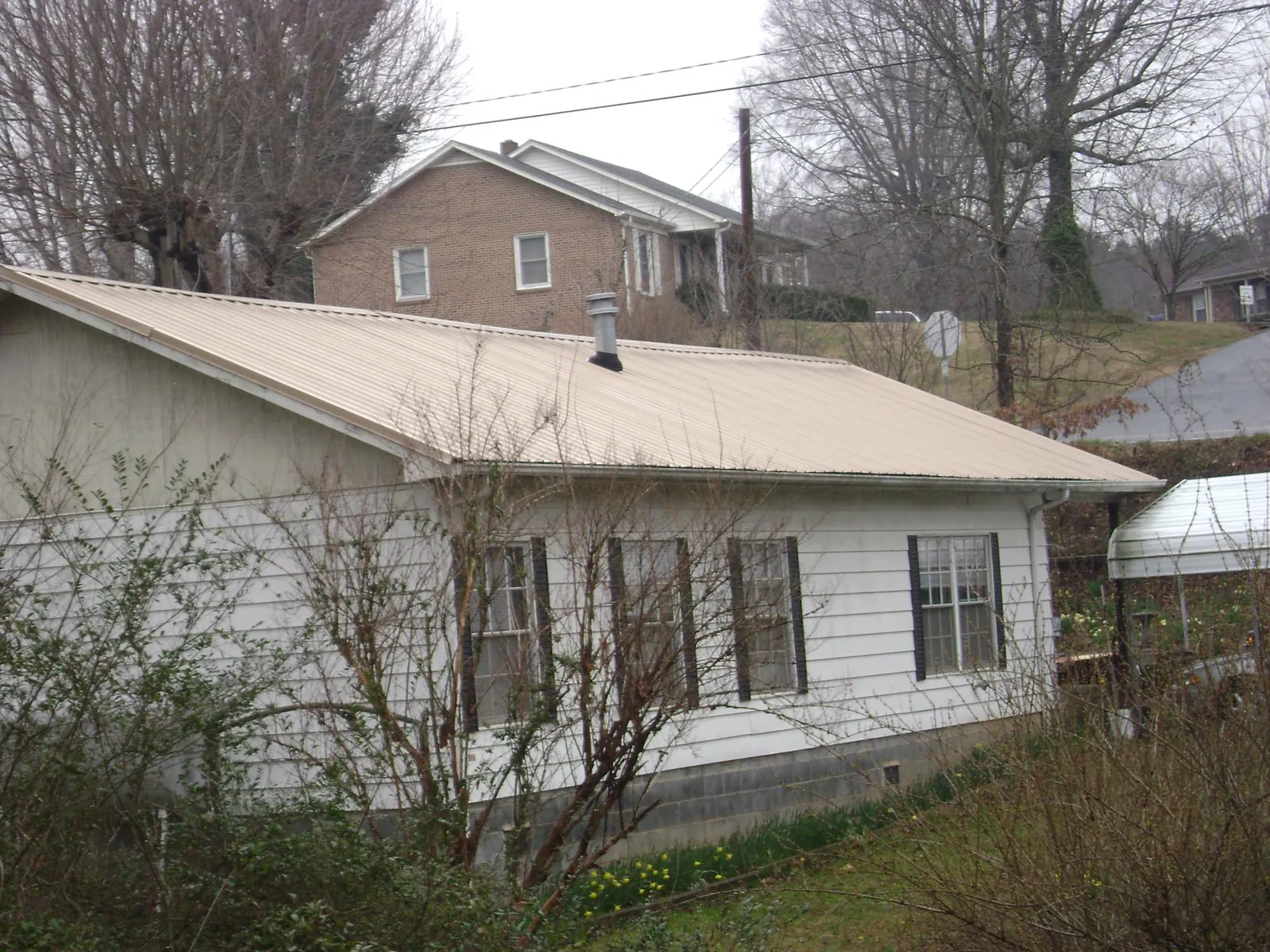 Tan metal roof on a white sided house set into a hillside — Commercial Roofing by Roofing Brothers in Cripple Creek